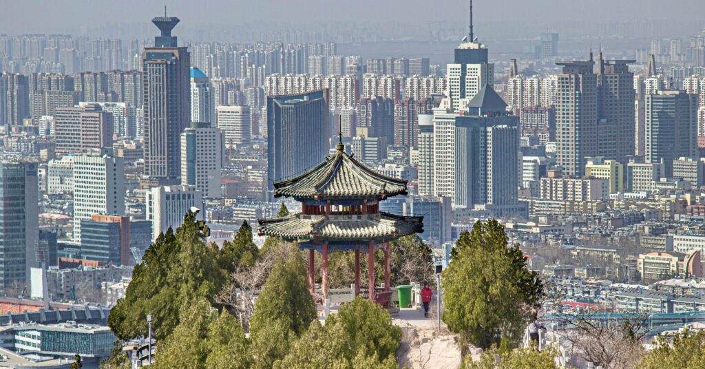 Elevated view of Jinan's skyline with traditional Chinese pavilion in the foreground.