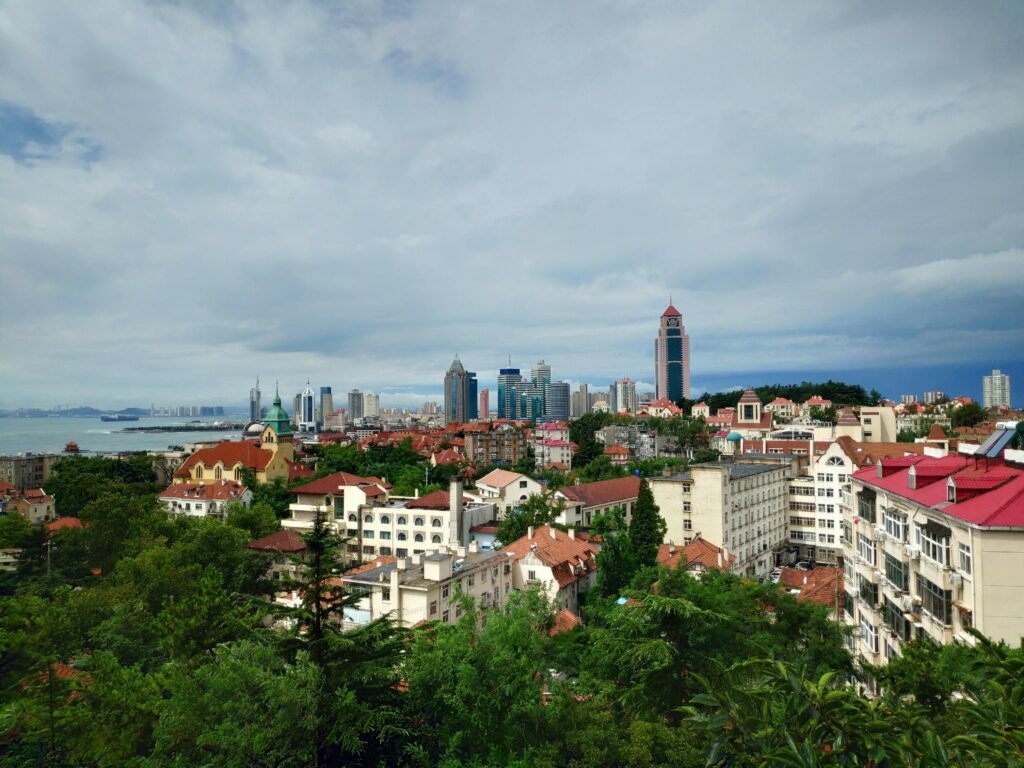 A scenic view of Qingdao's skyline with historical buildings and modern skyscrapers under a cloudy sky.