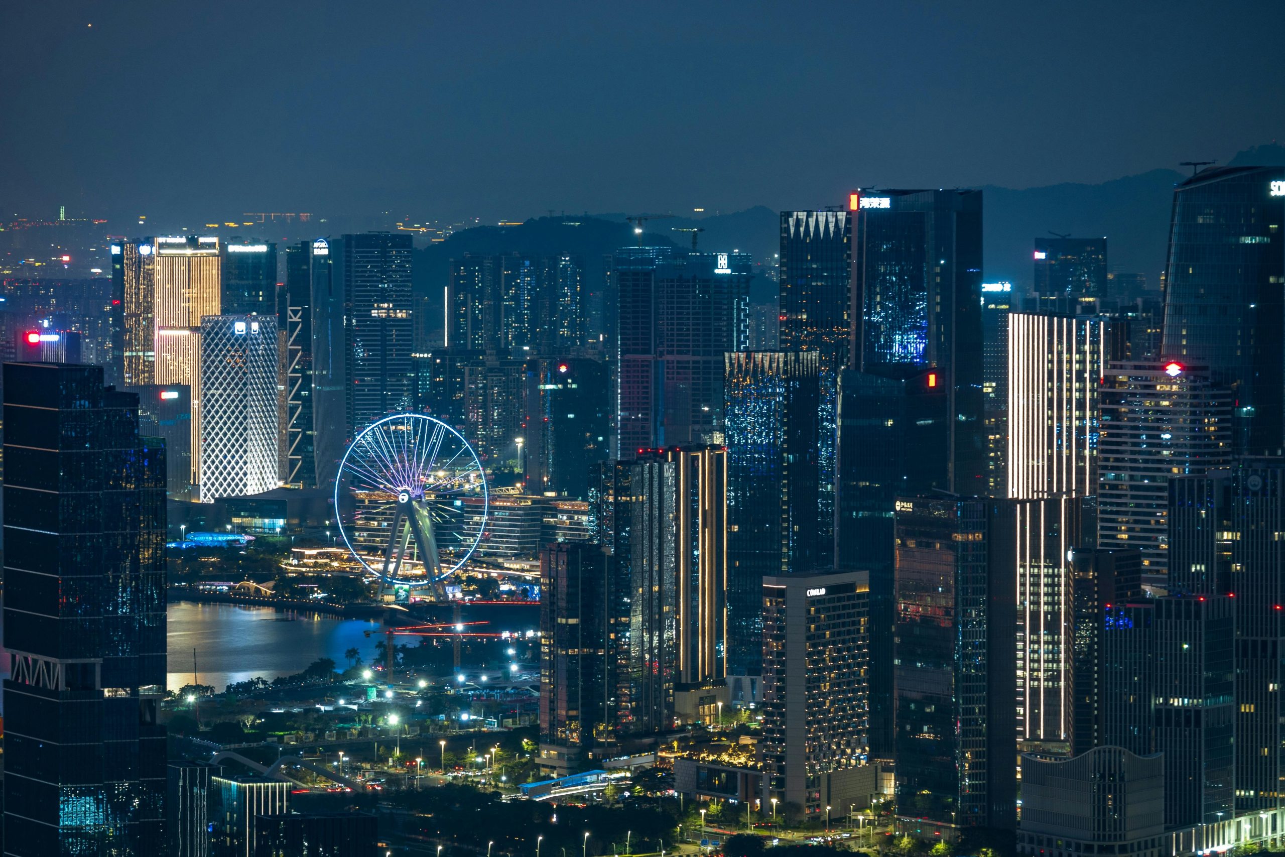 Dynamic city skyline illuminated at night featuring a striking Ferris wheel and skyscrapers.