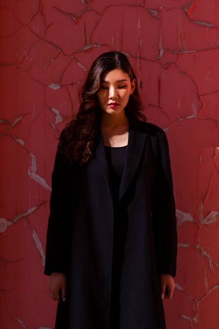 Stylish portrait of a woman in a black coat against a red cracked wall, showcasing elegance and fashion.