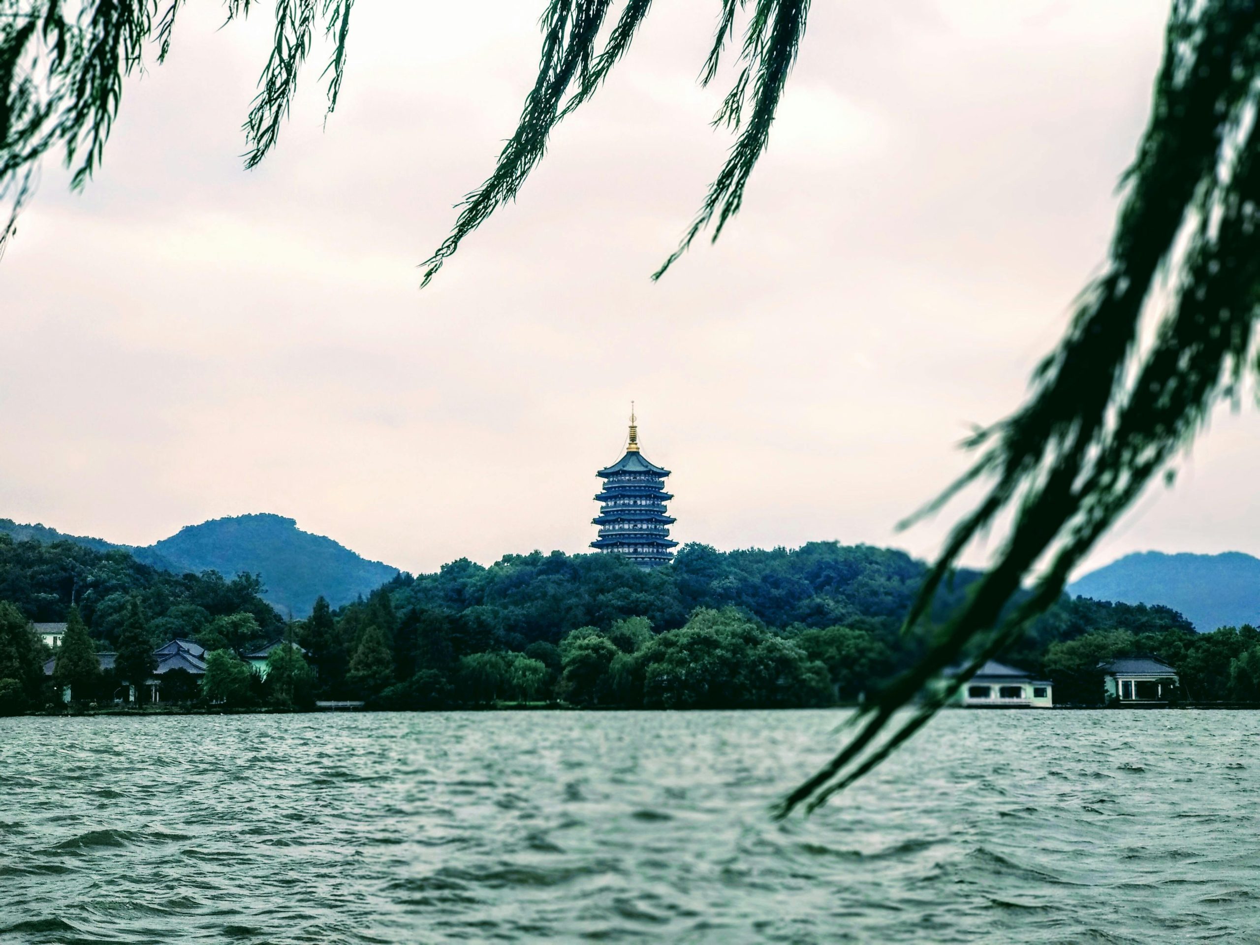 Scenic view of Leifeng Pagoda over West Lake, Hangzhou with lush greenery and tranquil waters.